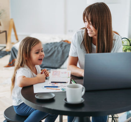 Working mom freelancer on the laptop with little daughter playing on the table together at home