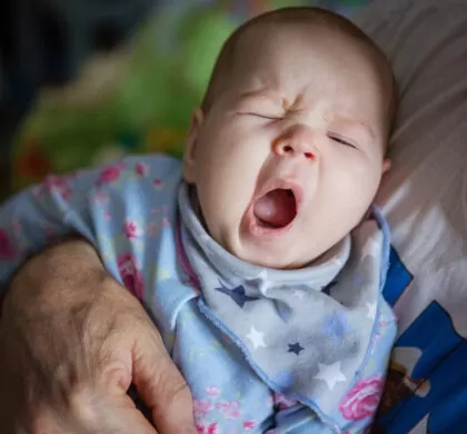 Baby girl yawning. Cropped view of grandfather rocking baby to sleep.