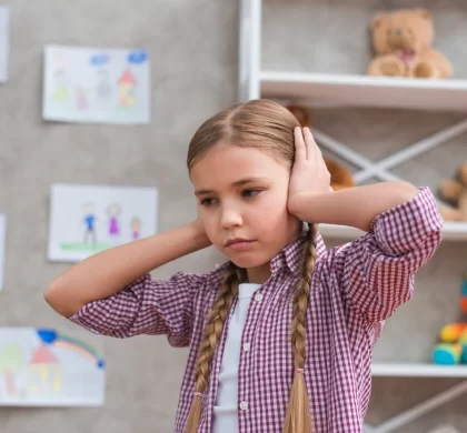 criança com ansiedade tapando os ouvidos em um quarto com desenhos na paredes e ursos na estante